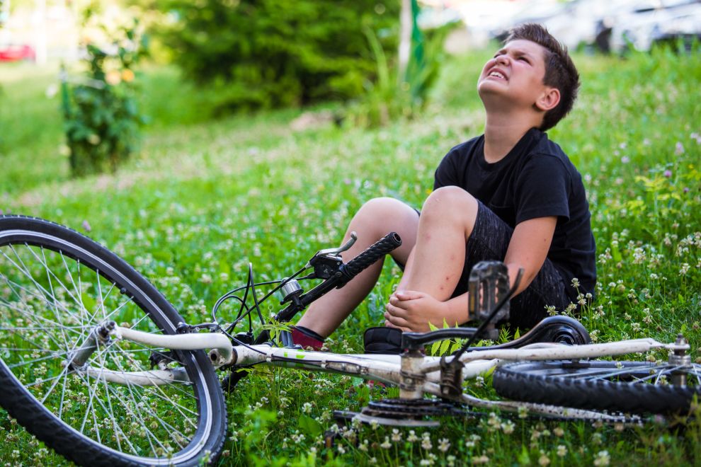 Fahrradunfall, Junge mit Schmerzen in den Kniegelenken nach dem Radfahren auf dem Fahrrad im Park. Knöchel schmerzt nach Fahrradsturz.