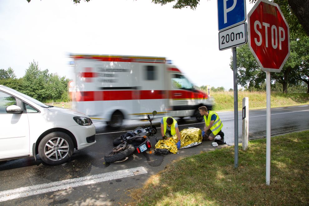 Erste Hilfe bei einem Motorradunfall, Ersthelfer vor Ort bedecken das Unfallopfer mit der Rettungsdecke.