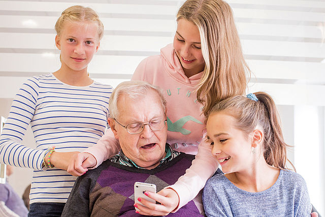 Gruppe Kinder zeigt einem Senior ein Smartphone-Handy