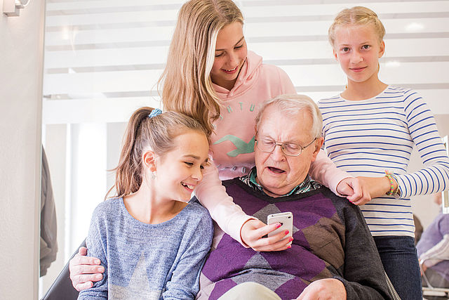 Gruppe Kinder zeigt einem Senior ein Smartphone-Handy