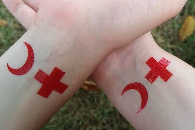 Zwei Handgelenke mit Tattoos aus roten Kreuzen und roten Halbmonden.