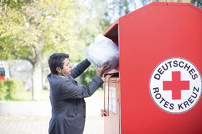 ein Mann wirft einen Spendensack in einen roten Kleidercontainer